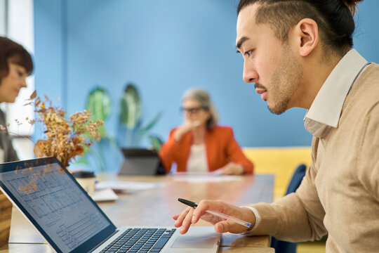 Architect analyzing blueprints on laptop in modern coworking office