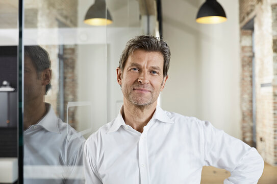 Portrait of smiling businessman leaning against glass pane