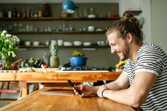 Young man with a bun sitting at home, using smartphone