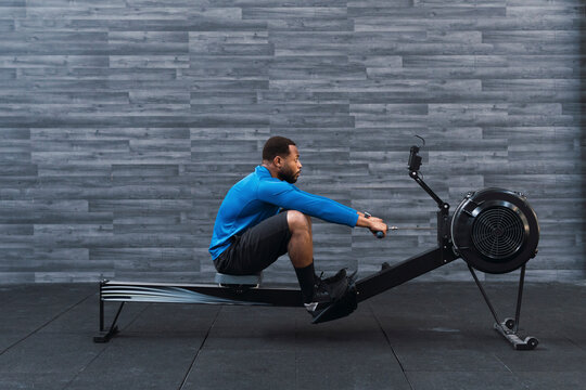 Concentrated athlete exercising on rowing machine in front of wall in gym