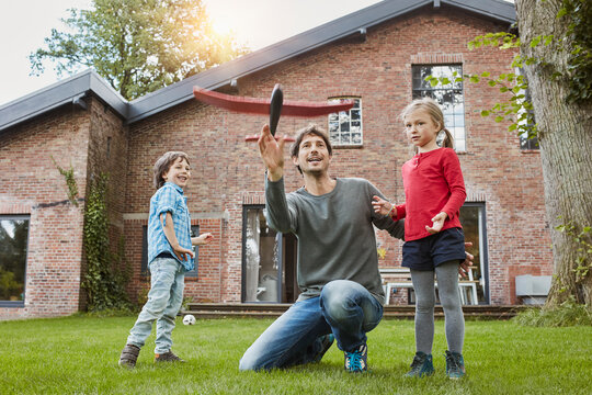 Father with two children playing with toy airplane in garden of their home