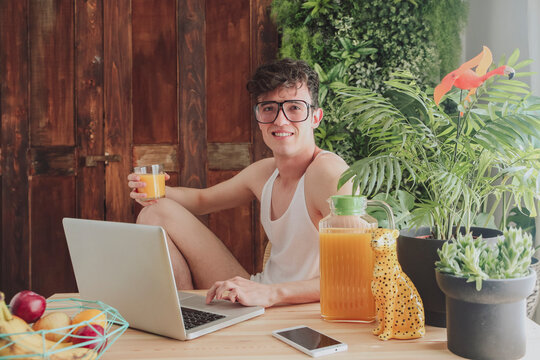 Young man using laptop and drinking orange juice at home