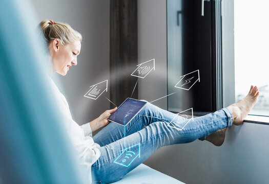 Woman sitting in office, using digital tablet to remote-control his smart home