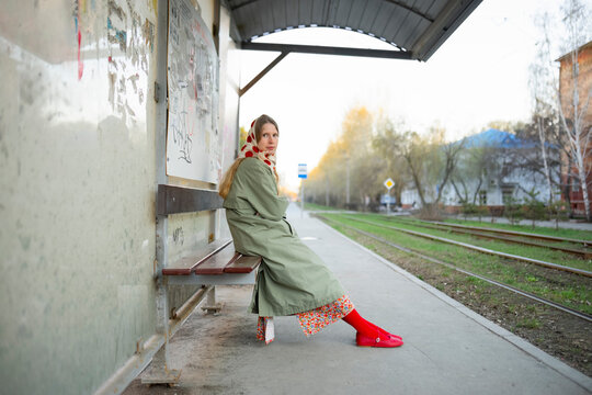 Passenger in raincoat and scarf waiting at tram stop
