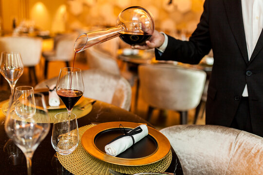 Waiter pouring wine from decanter into glass in fancy restaurant