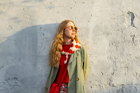 Smiling model in vintage raincoat against a wall at sunset