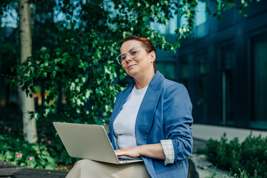 Professional working on laptop outdoors by modern city building