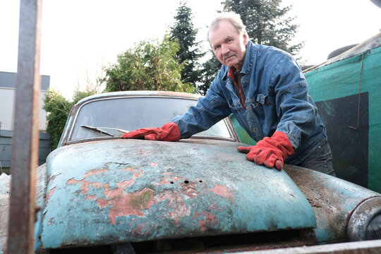 Mechanic resting on the hood of a rusty vintage car outdoors