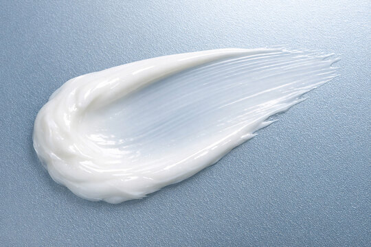 A close-up photograph of a thick white foamy liquid spilled onto a blue textured surface. The texture resembles waves or the underside of an object.