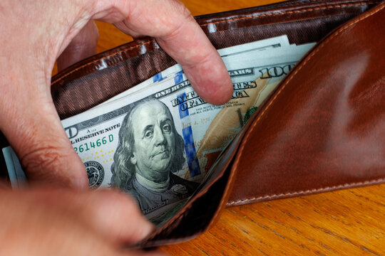 Hand taking a 100 dollar bill banknote from wallet, cost of living, wages, or inflation concept.