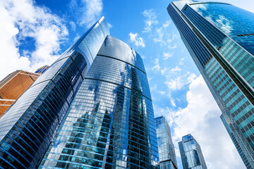 Naklejka premium Low angle view of modern glass skyscrapers in financial district. Contemporary corporate architecture symbolizing business, finance and urban development.