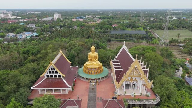 NAKHON PATHOM, THAILAND - Aerial forward drone shot approaching the giant golden Buddha statue at Wat Sam Phran Dragon Temple.