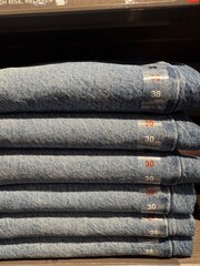 Stack of blue denim jeans on display shelf in retail store with size labels visible © dvoevnore