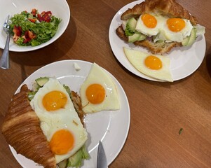 Breakfast croissant sandwich with fried eggs and avocado on white plates with fresh salad added. © dvoevnore
