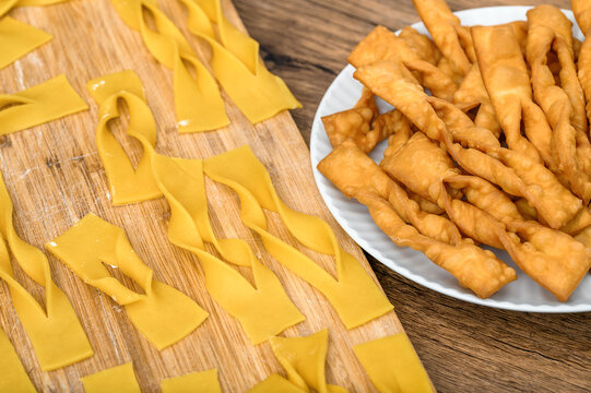 Raw angel wings before frying on a cutting board and fried on a plate, faworki chrusty