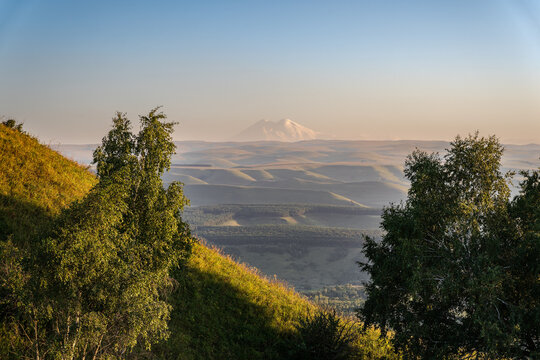 Panoramic view of the green valley and the snowy peak of Mount Elbrus on the horizon against the blue sky on a sunny clear morning in Kislovodsk Stavropol territory, Russia