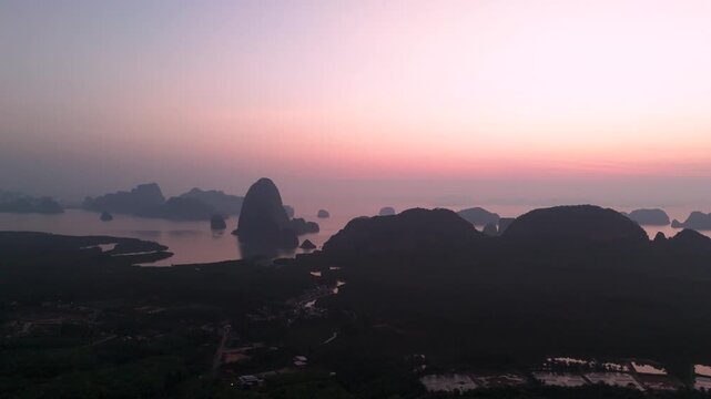 View from above Majestic limestone formations rise above emerald waters fringed by winding mangroves, vibrant coastal village of port is visible against the backdrop of an orange sunrise clouds