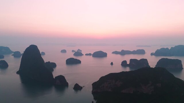 Aerial panorama wide view majestic limestone formations rise above emerald waters fringed by winding mangroves, with a bustling coastal village visible at orange sunrise