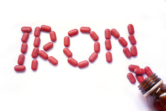 From the glass jar Iron supplement pills come out into the white background, Iron is used to treat anemia due to iron deficiency anemia. Iron written of red tablets.