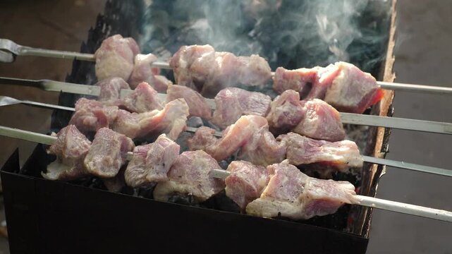 Appetizing pork shish kebab on metal skewers cooking on a mangal grill. The process of roasting juicy marinated meat over hot charcoals with thick smoke at a picnic