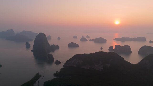 Aerial view majestic limestone formations rise above emerald waters fringed by winding mangroves, with a bustling coastal village visible at orange sunrise bright orange clouds.