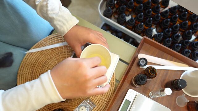 Top view of hands mixing natural ingredients in a preparation cup surrounded by essential oil bottles and formulation tools. Aromatherapy production, handmade cosmetics, wellness products and organic 