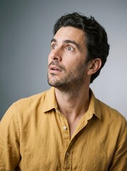 Obraz premium Man with dark hair gazes upward in mustard yellow shirt against gray studio background