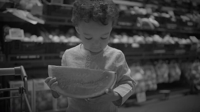 Child inspecting packaged lettuce in supermarket produce aisle, monochrome