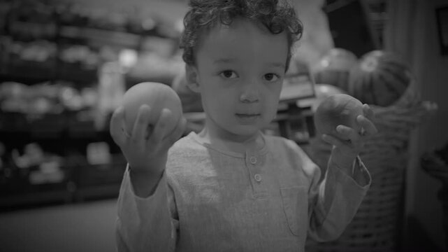 Toddler Standing in Supermarket Produce Aisle Holding Two Fruits