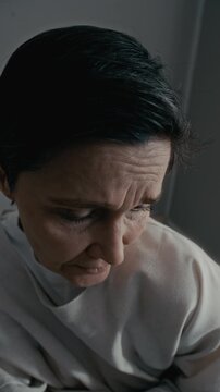 Vertical high angle portrait of middle aged Caucasian woman in straitjacket looking into camera. Footage is suitable for mental health awareness campaigns or psychiatric clinic promos