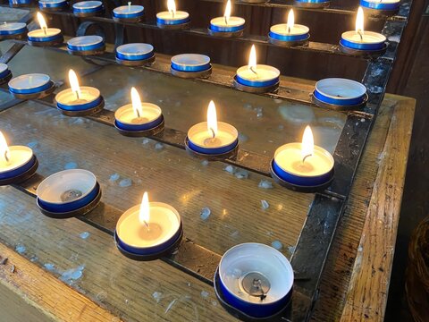 Rows of small candles burning in a church, lit in memory of loved ones. The warm candle flames create a peaceful and reflective atmosphere, symbolising remembrance, prayer, hope, faith, and eternal 