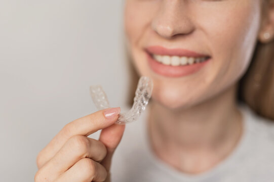 A woman holding clear aligners. Treatment for overbite, crowded teeth, and bruxism.