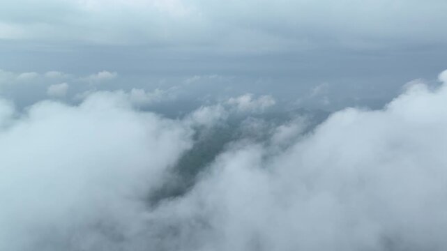 Aerial view flying through clouds revealing mountain landscape