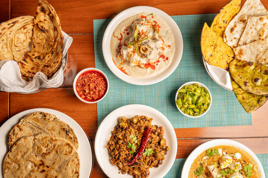 Top view of an authentic Rajasthani feast featuring Safed Maas, Nagori Paneer, Panchkuta Sabji, bajre ki roti, naan, missi roti, lehsun chutney, and mirchi ke gutte