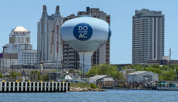 Skyline view of Atlantic City waterfront featuring a prominent water tower, casino hotels, harbor docks and urban buildings under a clear blue sky, conveying travel, tourism and coastal city life.