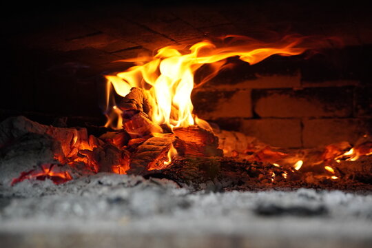 Traditional wood fired stone pizza oven with refractory dome interior, close-up fire texture