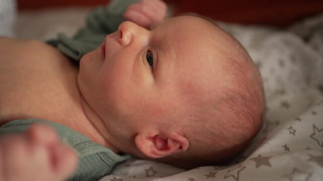 Adorable newborn baby waking up from sleep, opening its big curious eyes and looking around with a gentle expression. The infant lies comfortably in a cozy crib, alert and happy
