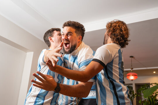 Grupo de amigos argentinos celebrando un gol mientras ven un partido de f&uacute;tbol