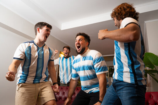 Grupo de amigos argentinos celebrando un gol mientras ven un partido de f&uacute;tbol