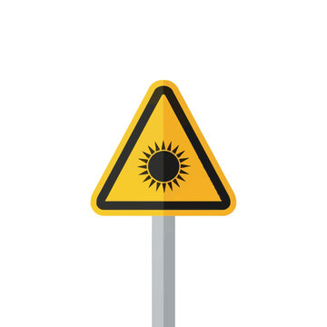 Yellow triangular warning sign with a black sun symbol indicating optical radiation or solar hazard, mounted on a grey pole against a white background for safety communication.