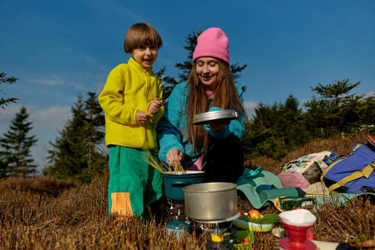 Mother and child cooking pasta on camping stove outdoors