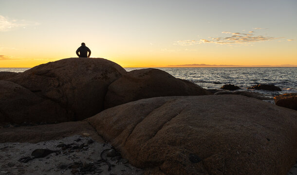silhouette of man viewing sunrise atop boulder rock, Saldanah Bay, Western Cape, South Africa