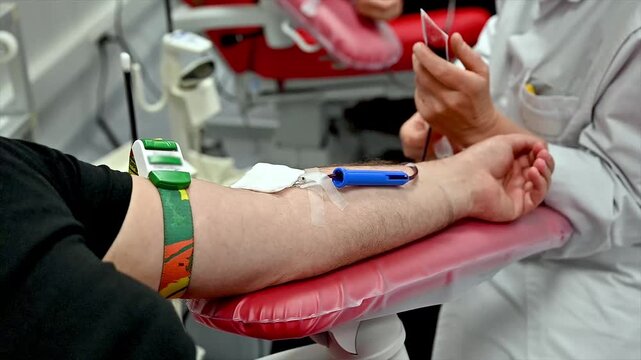 Close-up of a nurse inserting a needle into a blood donor arm and holding a sample tube at a clinic illustrating venipuncture and blood sample collection during donation.