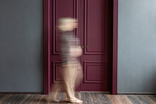 A pregnant woman walks past a closed door.