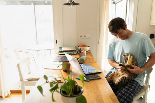 Man Sits at Desk With Cat in a Home Office in the Morning