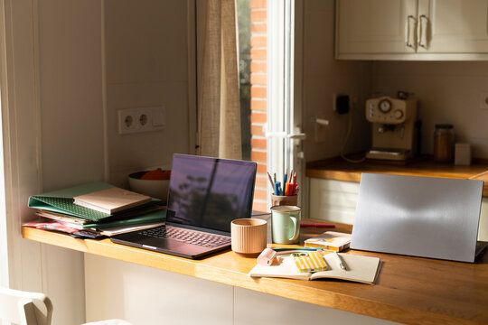 Workspace With Laptop, Notebooks, and Coffee in a Kitchen Area