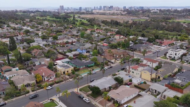 Scenic landscape over a suburban neighborhood of houses and streets with downtown San Diego skyline background, urban sprawl development