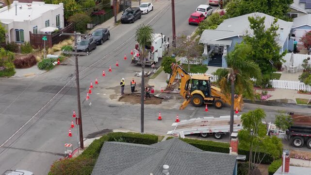 Construction workers repairing residential street with backhoe and traffic cones in San Diego, California. Overhead point of interest of urban infrastructure project