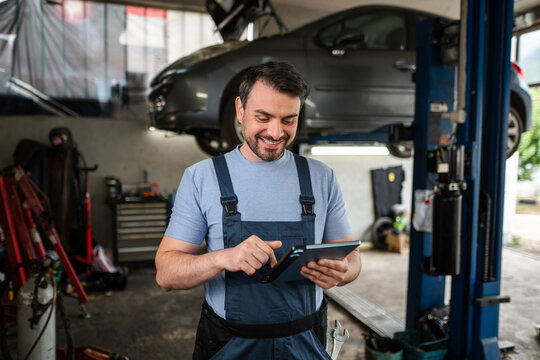 Car mechanic using a tablet in a workshop with a lifted car