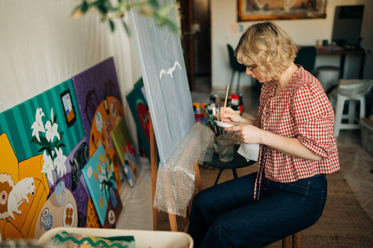 Woman artist mixing paint on palette while sitting at easel